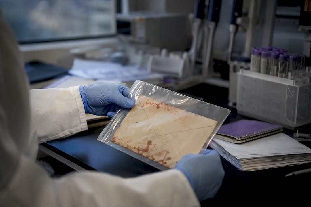Gloved hands holding bloodied envelope in lab